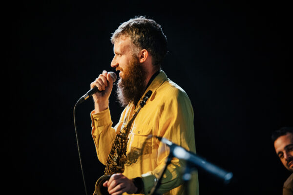 A white man with a beard and wearing a yellow shirt speaks into the microphone.