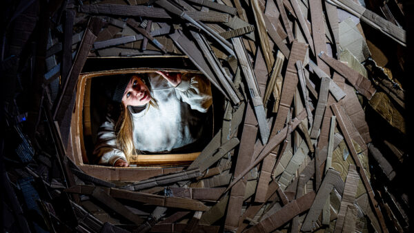 A girl in a white light leaning over a window made out of wood.