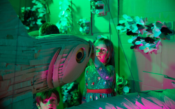 A young girl in a flowery dress touching an animal crafted from cardboard