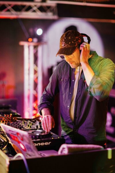 A white man wearing a cap djs with headphones to his ear