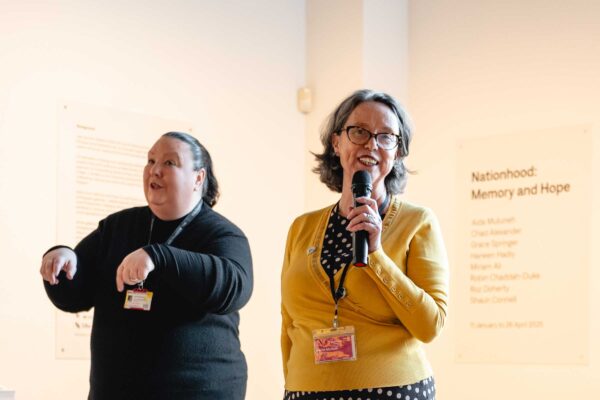 A woman talks into a microphone with a female BSL interpreter to her right