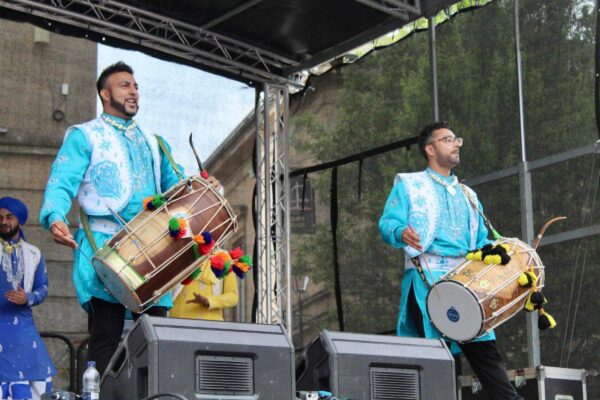 Two men in traditional Indian dress play dhol drums on stage