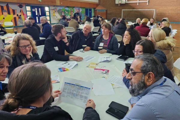 a group of people sit around a table, talking and looking at leaflets