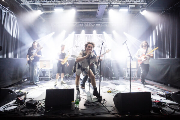 A band performs on stage - backlit by white lights.