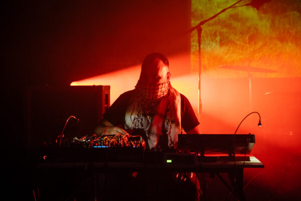 A person sits behind a table playing on DJ decks, backlit by red lights.