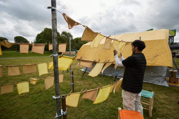 A man puts out small yellow squares on a washing line outside the tent.