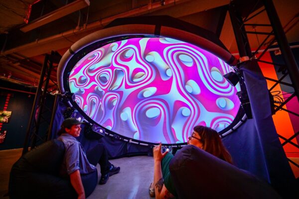 Two people looking up at a circular projection of blue and pink waves