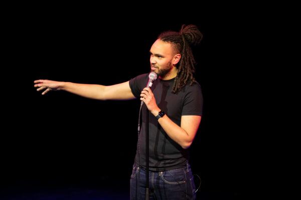 Comedian Alex Dunlop performs holding a microphone.