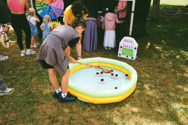 A film photo of a young person hooking a sheep floating in a kiddie pool of water.