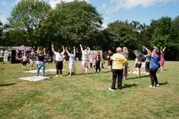 A film photo of people dancing in a park, surrounded by green trees