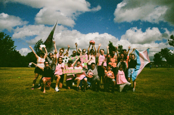 A film photo of people on a football team, all wearing a pink kit and waving flags.