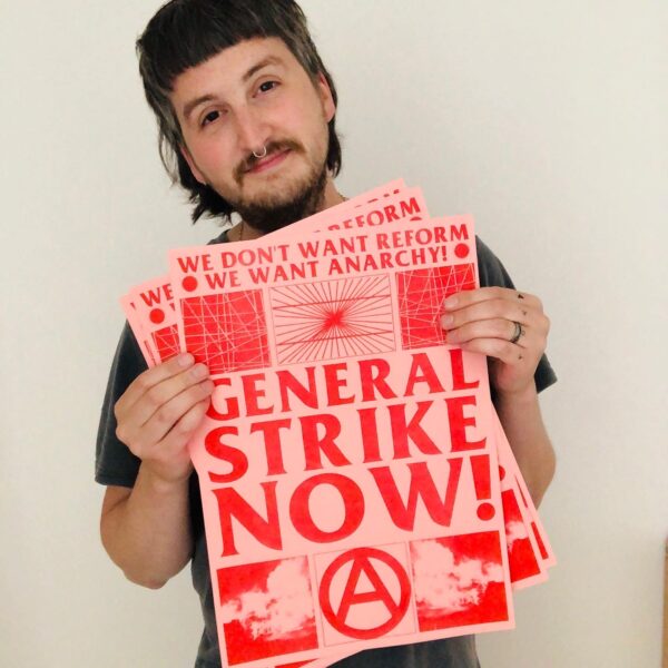 A person with brown hair and a beard poses from the camera - showing a pink and red poster.
