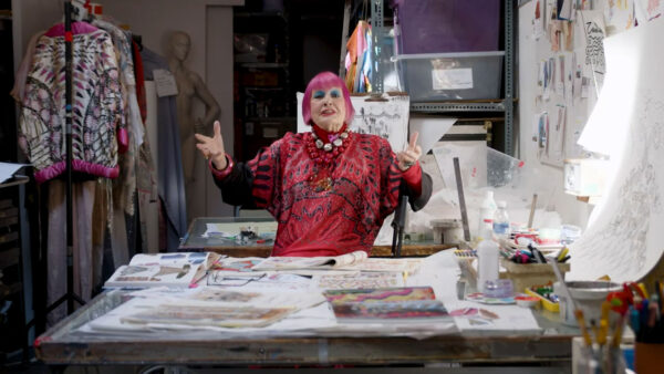 Designer Dame Zandra Rhodes stands in her studio surrounded by drawings.