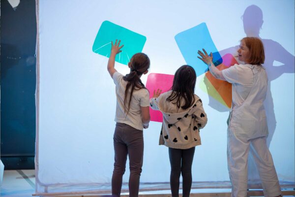 Three people place their hands on coloured squares on a screen