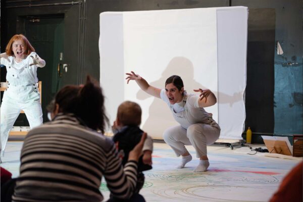 A woman crouches in an imposing position on a giant piece of paper covered in paint