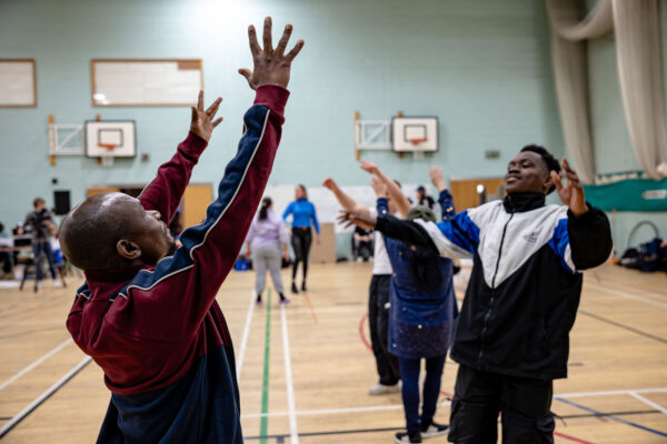 Participants in a movement workshop raise their hands in the air.