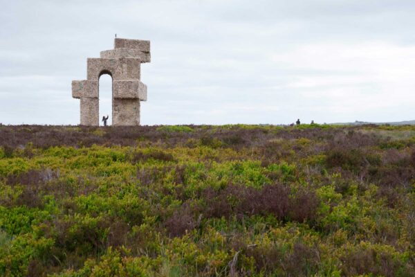 The artwork Tower by Steve Messam, in the landscape of Penistone Hill. The large sculpture is covered in sheep fleece, creating the shape of an arch with angular corners, set against a cloudy sky and the natural landscape.