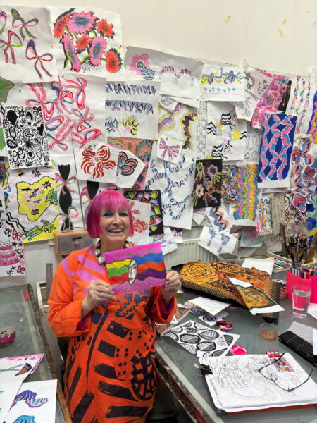 Designer Dame Zandra Rhodes stands in her studio surrounded by drawings.