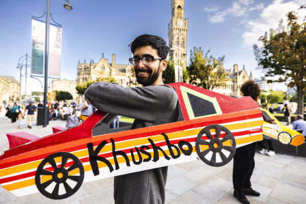 Male with red and orange cardboard car slotted over his body.