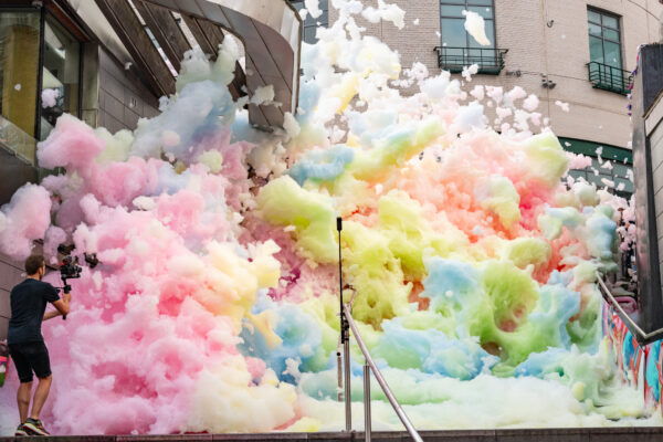 Multi-coloured foam crashing down some steps outside. Man with a video recorder stood to the left of the image.