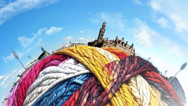A giant ball of colourful yarn with the Bradford skyline around the edge of it against a blue sky.