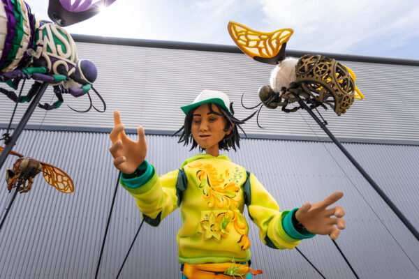 Puppet, Zee, wearing a yellow tracksuit top. Interacting with three bees that are on the end of poles.