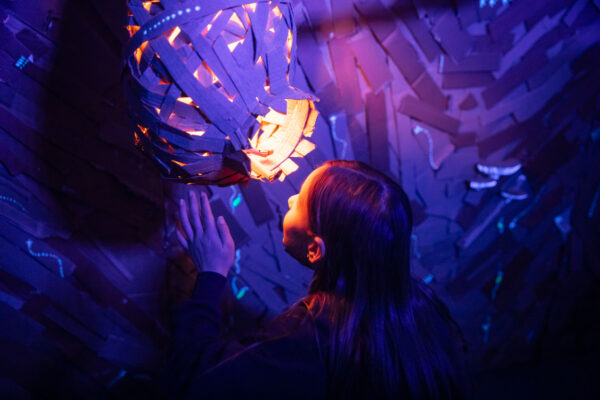 A child looks into a cardboard sculpture, with a light shining from it onto her face.