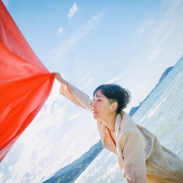 Person stood in-front of the ocean dancing, holding red material.