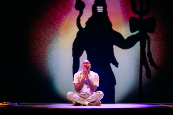 man sat cross legged on the floor with hands in prayer, with a shadow behind him