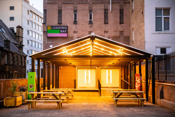 The entrance to Loading Bay, with rows of benches under a canopy light by warm light.