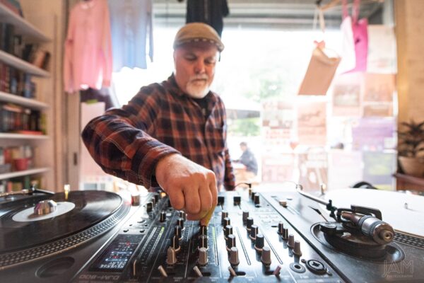 Man wearing flat cap tuning on DJ controllers.