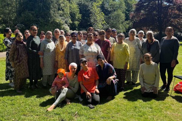 A large group of people in traditional Sikh dress pose for a picture in a park.