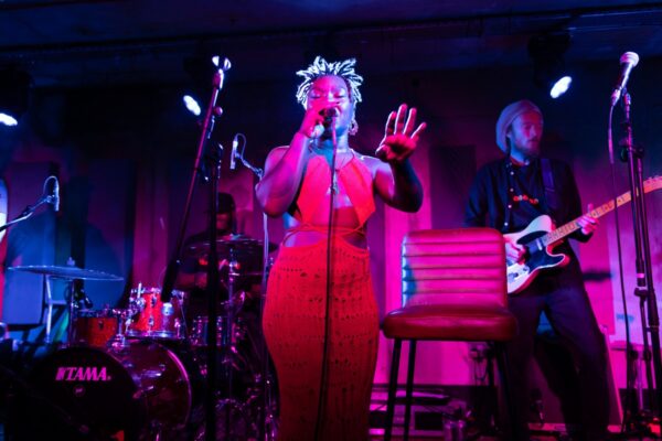 Woman stood on a stage singing. The microphone is in front of her and the stage light is behind her, making a slight silhouette.