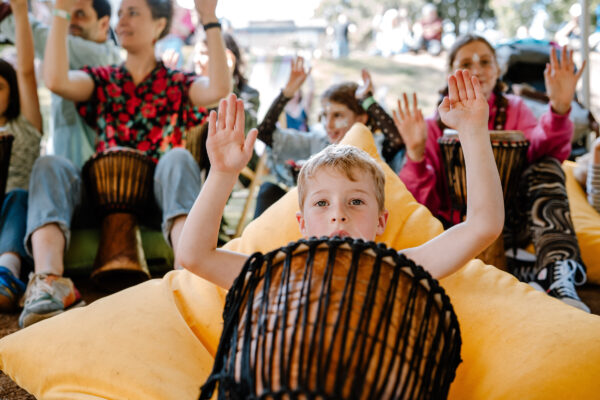 Young person sat on a bean bag with drum in front of them with hands above their head