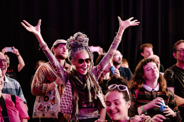 Woman in crowd with hands open above her head, looking happy