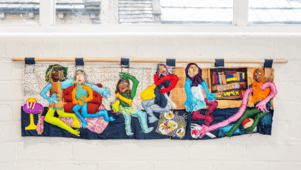 a large hung textile fabric piece depicting women relaxing in a living room space.