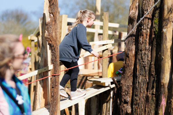 Child balancing on a beam of wood while holding on a rope.