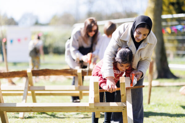Mother and daughter leaning over a piece of wood, sawing pieces off.