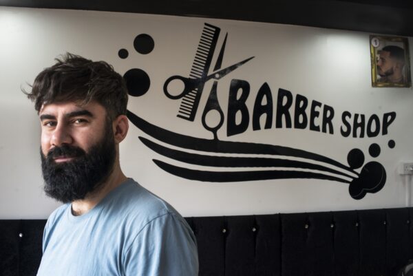 Man posing infront of his barber shop sign