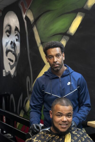 two men, one is sat in a barber chair