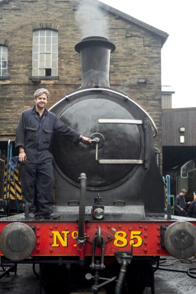 man stood infront and on a steam train