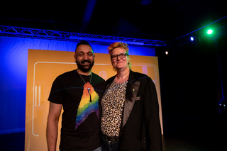 Two people pose in front of an orange sign.