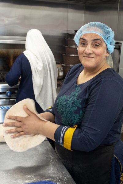 Lady smiling in a kitchen with a hair net on and a flat bread in her hands
