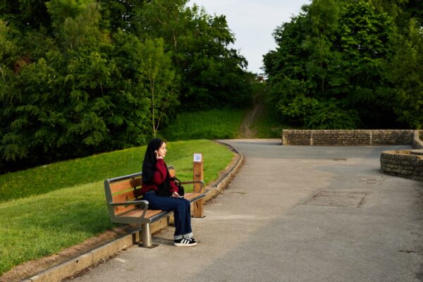 A girl listening to something, sat on a bench outside