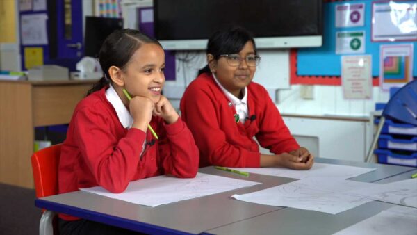 Two children in red school jumpers sitting in a clasroom doing an art activity.