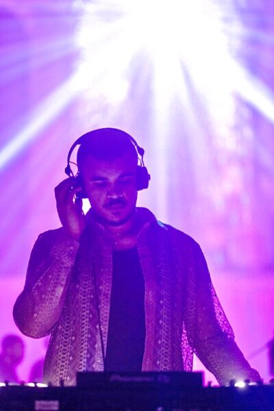 A man plays the DJ decks - backlit by purple light, with headphones on his head