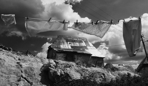 A black and white image of washing on a line, above a barn building.