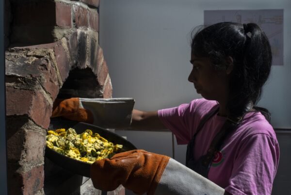 Ajeema putting vegetables into a wood fired oven. People harvesting food from the allotments at NEET (the Northcliffe Environmental Enterprise Team) in Northcliffe Park, where they meet several times a week. They then prepare what tehy have picked to make a lunch which they share. Photo by Tim Smith.