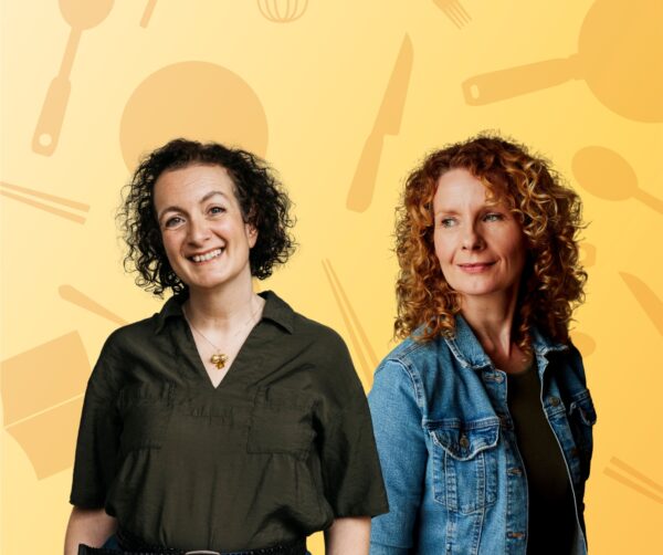 Two ladies smiling and posing, one has brown curly hair and the other has curly ginger hair.