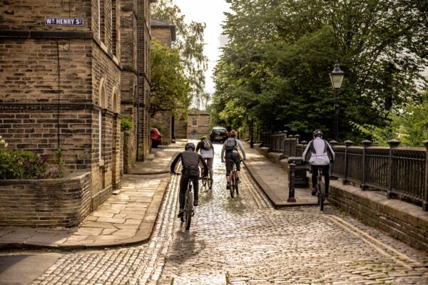 people cycling up hill on cobbled streets in saltaire